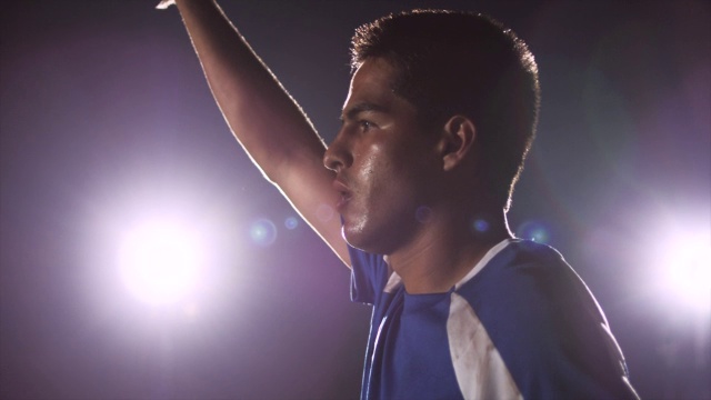 潘特写流汗的男子足球运动员站在球场上;他举起手臂，跑出球门(背景有聚光灯)视频下载