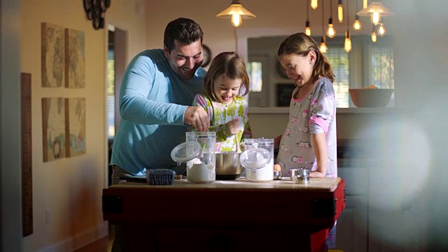 WS。爸爸穿着睡衣做早餐，一边和女儿们一起搅拌煎饼面糊，一边玩得很开心。视频素材