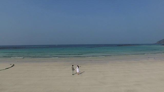 在济州岛的海滩上，一对夫妇手牵手散步的鸟瞰图视频素材