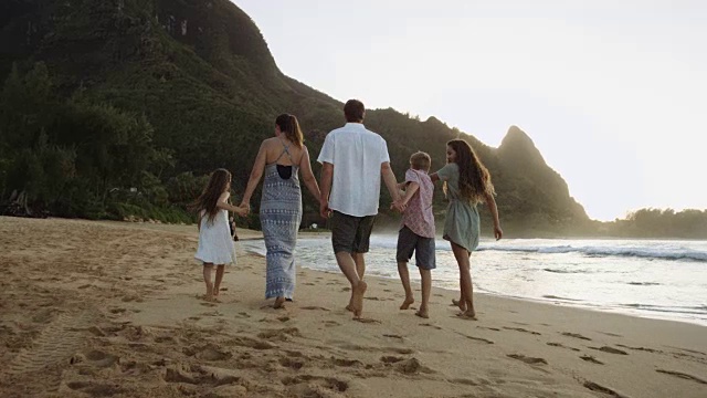 日落时分，一个白人家庭牵着手在海滩上散步视频素材
