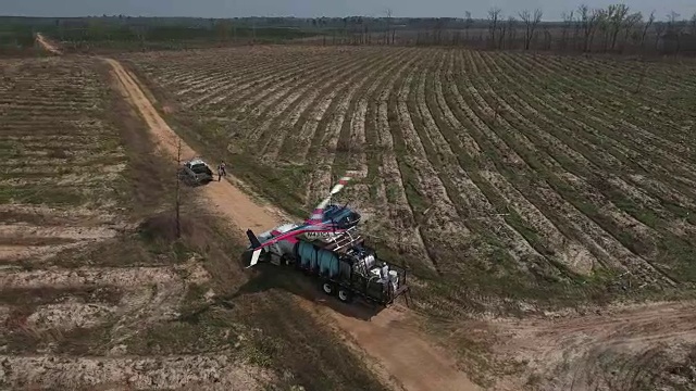 直升机在卡车上的轨道与guy工作-无人机空中4K空中拍摄特技直升机喷洒农药和杀虫剂在作物和树木上生产各种需要4K运输视频下载