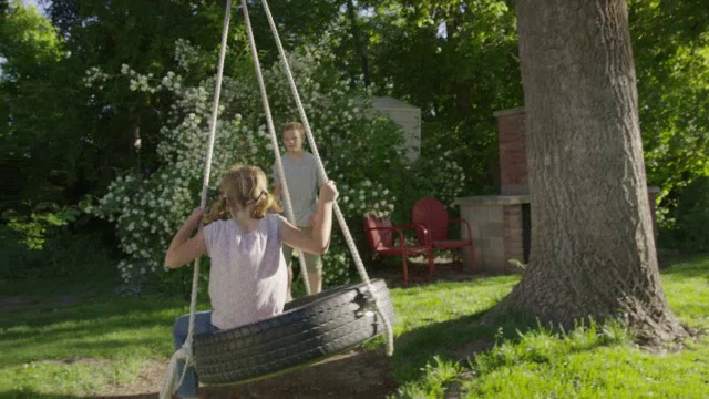 宽镜头男孩推女孩在轮胎秋千/斯普林维尔，犹他州，美国视频素材