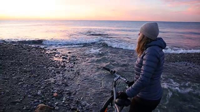 日出时分，一名女子在海滩河边推着自行车视频素材