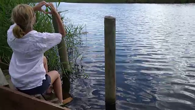 年轻女子坐在河边做心形框架视频下载