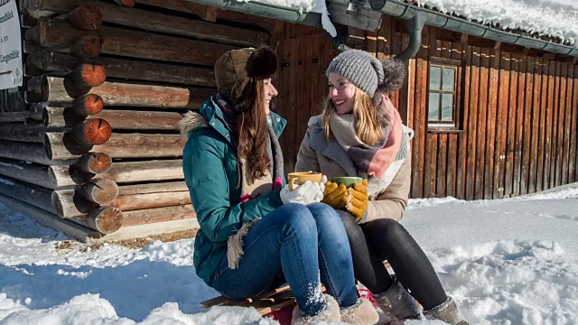 我们年轻的女人在一个小木屋前喝着热茶在冬天视频素材