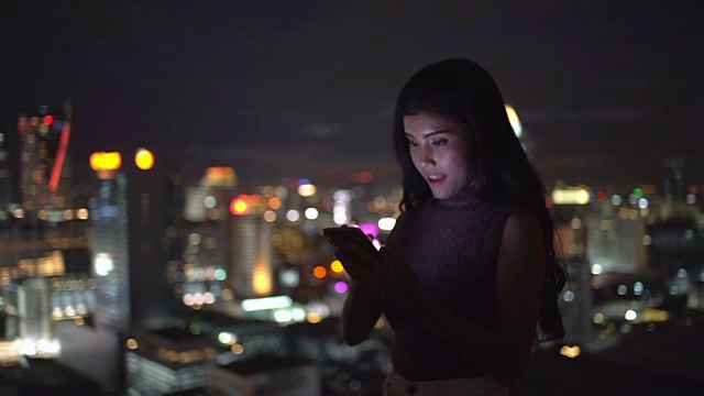 女人使用智能手机非常开心的交流包括连接她的朋友，看有趣的视频，电子邮件，聊天和网上购物在城市晚上:万向镜头视频素材