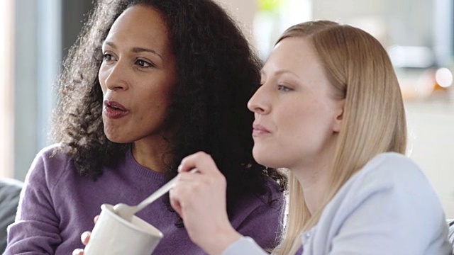 两个女性朋友一边吃冰淇淋一边看电视视频素材