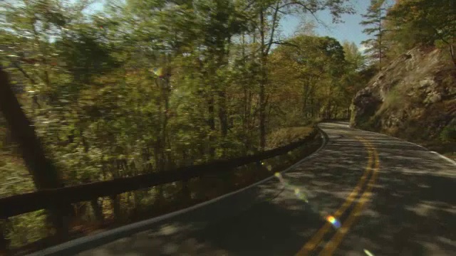 在晴朗的蓝天下，一条山路蜿蜒穿过五颜六色的秋叶。视频下载