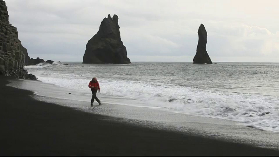 一名男子在冰岛南部海岸维克附近的黑色火山沙滩上躲避海浪。视频素材