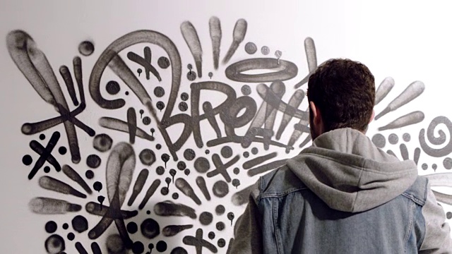 SLO MO。年轻艺术家喷涂黑色X和离开涂鸦壁画在白色工作室。视频下载