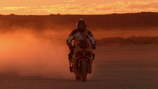 宽镜头人驾驶和减慢摩托车在沙漠黄昏/加利福尼亚视频下载