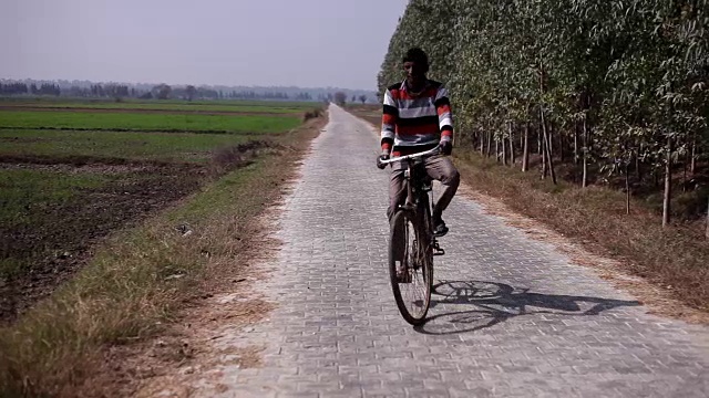 农民骑自行车在绿色的田野附近的自然视频素材