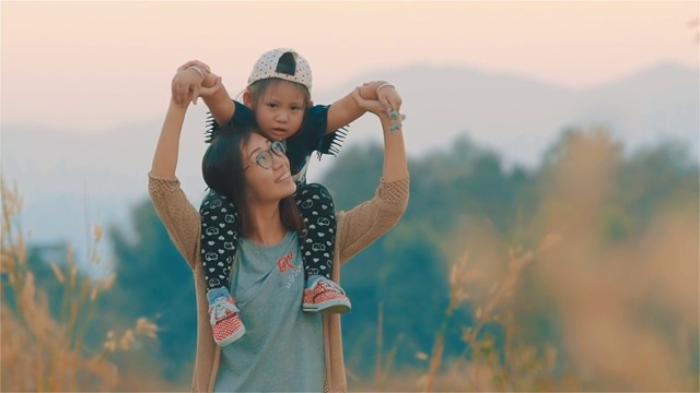 快乐的亚洲年轻妈妈背着女儿一起在朦胧的田野里视频购买