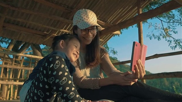 亚洲年轻的母亲和女儿坐在大自然中，在户外用智能手机进行视频通话视频素材