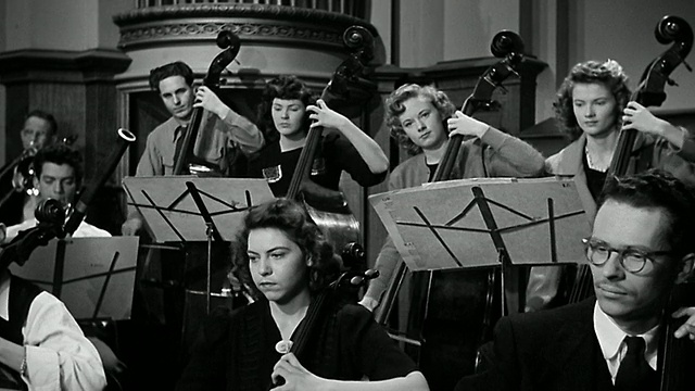 20世纪40年代的宽镜头音乐家在管弦乐表演中演奏低音提琴和大提琴视频素材