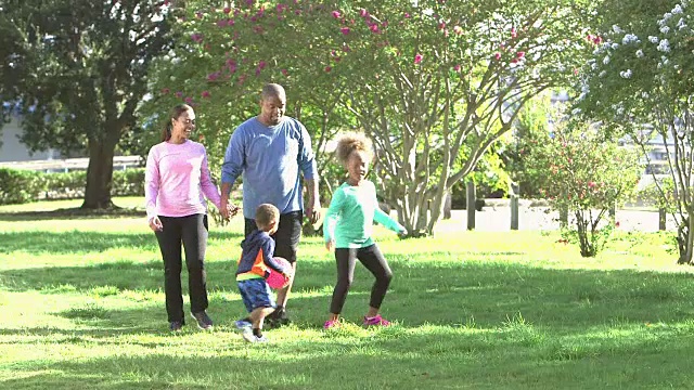 一家人在公园里，父母手牵着手，孩子们在跑步视频素材