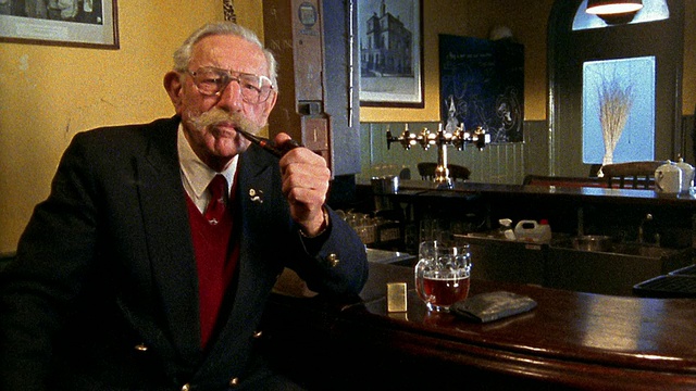 一个中等口径的老人在酒吧里抽着烟斗，旁边放着一杯啤酒视频素材