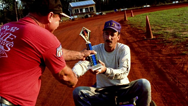 中程跟踪射击手将奖杯赠与坐在割草机上的其他男子，获胜者将奖杯/阿拉巴马州视频下载