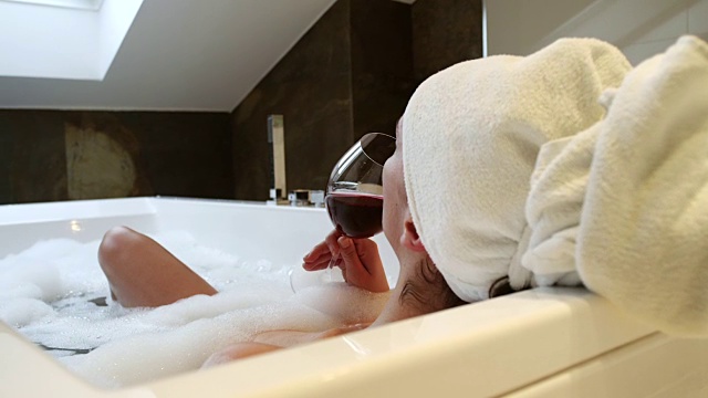 放松的女人在浴缸里喝葡萄酒视频素材