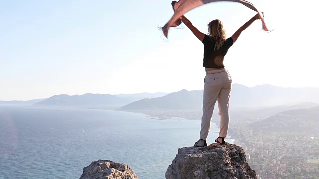年轻女子高举着围巾，在海上的岩石上视频素材