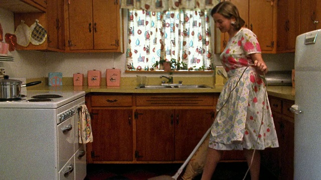 远景重现主妇在厨房用吸尘器吸油毡地板时微笑视频素材