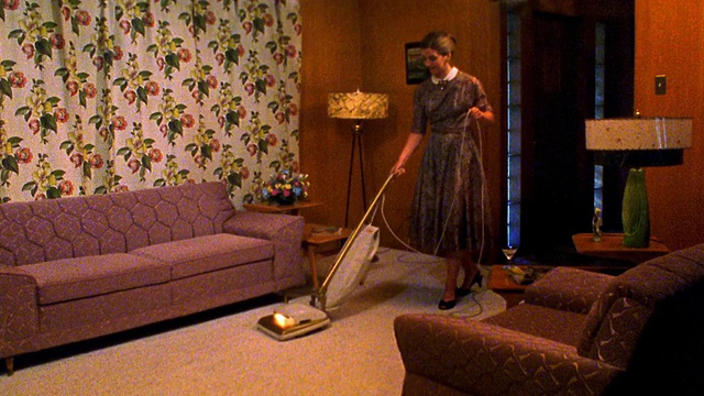 广角镜头再现女人用吸尘器打扫客厅，停止和喝鸡尾酒杯，而微笑视频下载