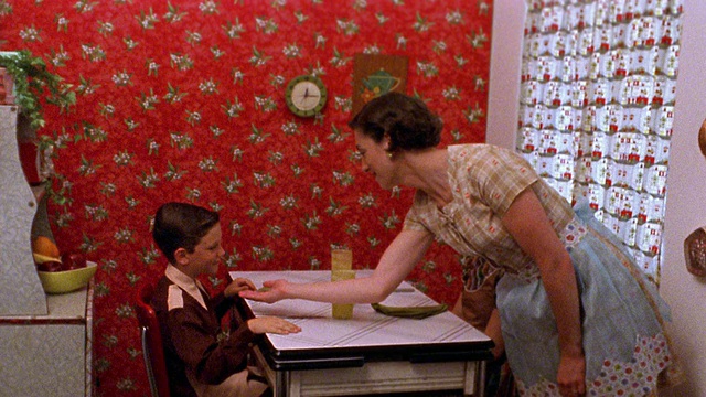 中景再现:女人伸出手让男孩吐口香糖，而女孩在厨房的桌子上看视频素材