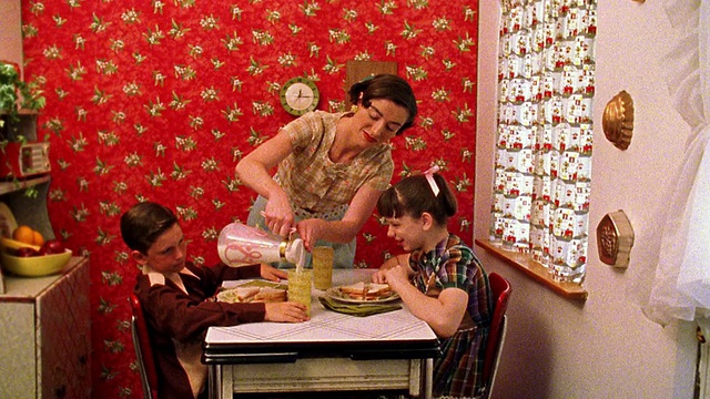 中镜头再现了一位妇女在厨房的餐桌上为男孩和女孩端上三明治，然后从罐子里倒牛奶视频素材