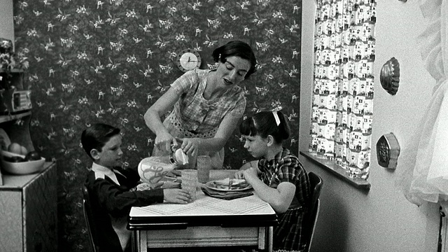 中镜头再现了一位妇女在厨房的餐桌上为男孩和女孩端上三明治，然后从罐子里倒牛奶视频素材