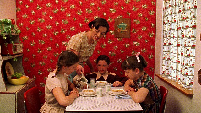 中镜头再现了一位妇女在厨房餐桌上将牛奶倒进孩子们的麦片碗里的场景视频素材
