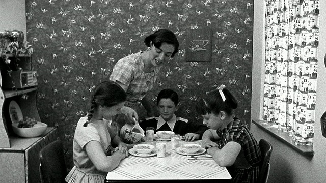 中镜头再现了一位妇女在厨房餐桌上将牛奶倒进孩子们的麦片碗里的场景视频素材