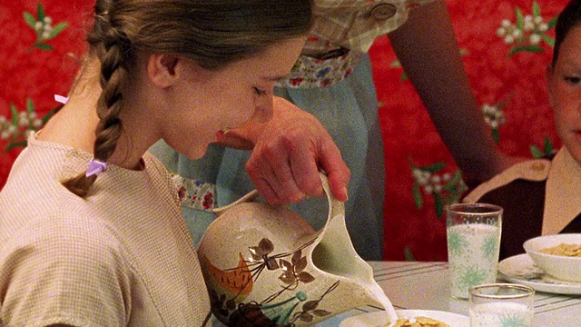 近距离跟踪拍摄——在厨房桌子上，一位妇女用手将牛奶倒进孩子们的麦片碗里视频素材
