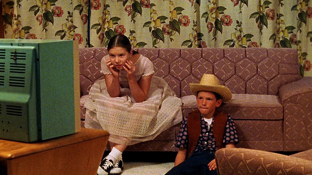 中景重演女孩和男孩的笑声+指着坐在客厅的电视前/男孩戴着牛仔帽视频下载