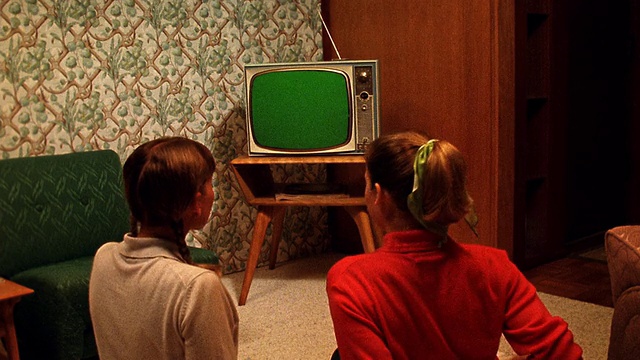 中景REENACTMENT 2少女坐在地板上看电视在客厅/电视屏幕是绿色的使用色度键视频下载