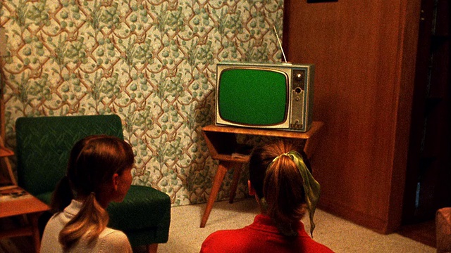 中景REENACTMENT 2十几岁的女孩坐在地板上看电视在客厅/电视屏幕是绿色的使用色度键视频下载