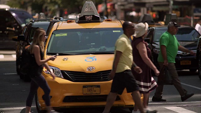在一个阳光明媚的日子，出租车和乘客在繁忙的纽约街道的人行横道上等待。视频素材