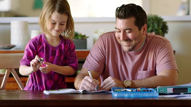 年轻的爸爸和女儿笑了，并用魔法笔在笔记本上画有趣的图画。视频素材
