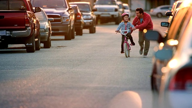 小女孩在附近的街道上骑着自行车，爸爸在旁边教她如何骑车。视频下载