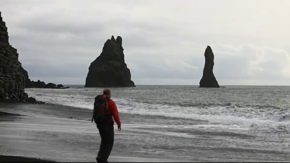 一名男子在冰岛南部海岸维克附近的黑色火山沙滩上躲避海浪。视频素材