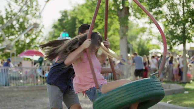 中等镜头的男人旋转女人在游乐园/愉快的树林，美国犹他州视频下载
