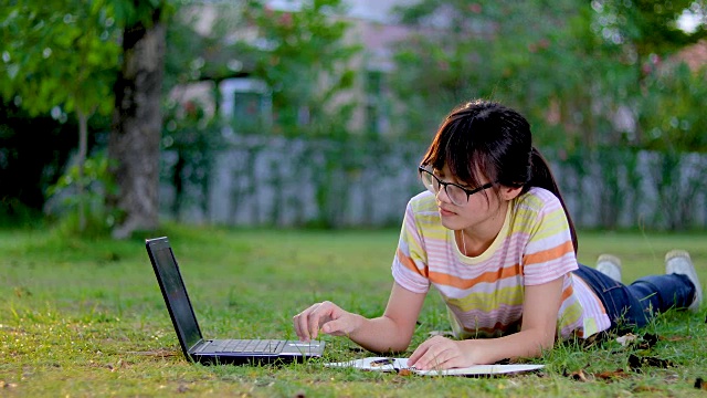 微笑的亚洲女孩在公园的树下与平板电脑视频下载