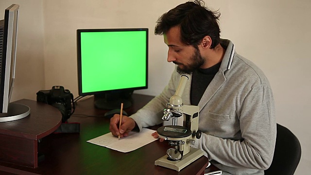 一个人用一个显微镜和一台有两个显示器的电脑工作视频下载