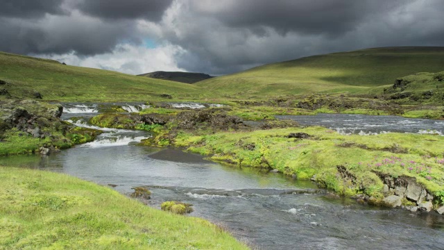 宽摇拍摄的河流流经起伏的景观/冰岛视频下载