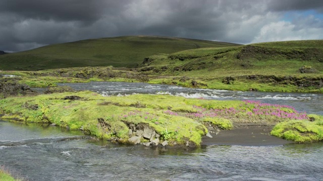 宽摇拍摄的河流流经起伏的景观/冰岛视频下载