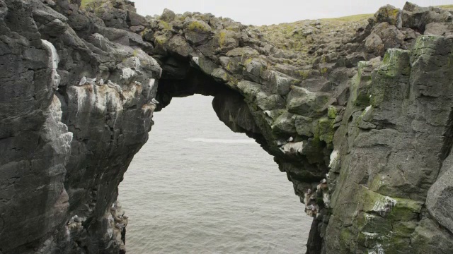 冰岛，Snaefellsnes, Arnarstapi，大范围的起重机拍摄鸟类在拱形岩层附近飞行视频下载