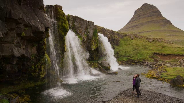 在冰岛Snaefellsnes瀑布/ Grundarfjorour附近，男人拍摄女人的宽平移镜头视频素材