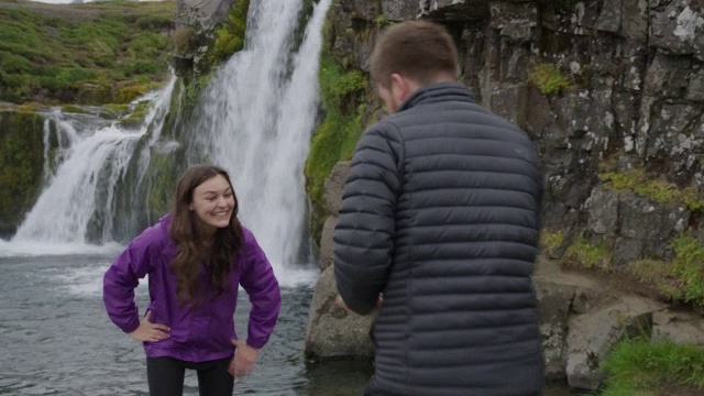 在冰岛Snaefellsnes, Grundarfjorour瀑布附近，男子拍摄女子的中等平移镜头视频素材