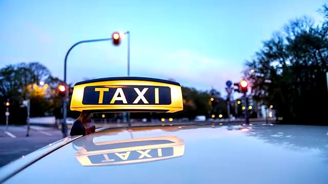 汽车上的一辆车长曝光时间流逝操纵拍摄的一辆德国出租车。出租车顶标志/大泽臣在前景。黄色驾驶室的车顶表面反射着条纹。背景是运动模糊和城市灯光是条纹。视频素材