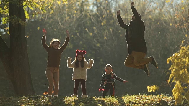 好玩的家庭跳跃与高举的手臂，并有乐趣在秋天的一天。视频素材