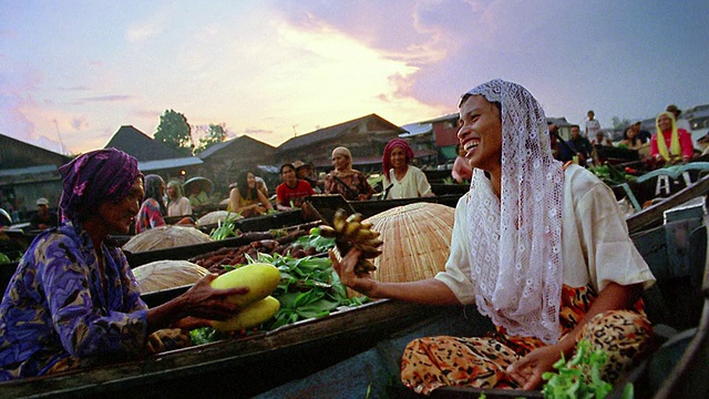 在印度尼西亚河上的水上市场上，小船上的女商贩在交换水果和蔬菜视频下载